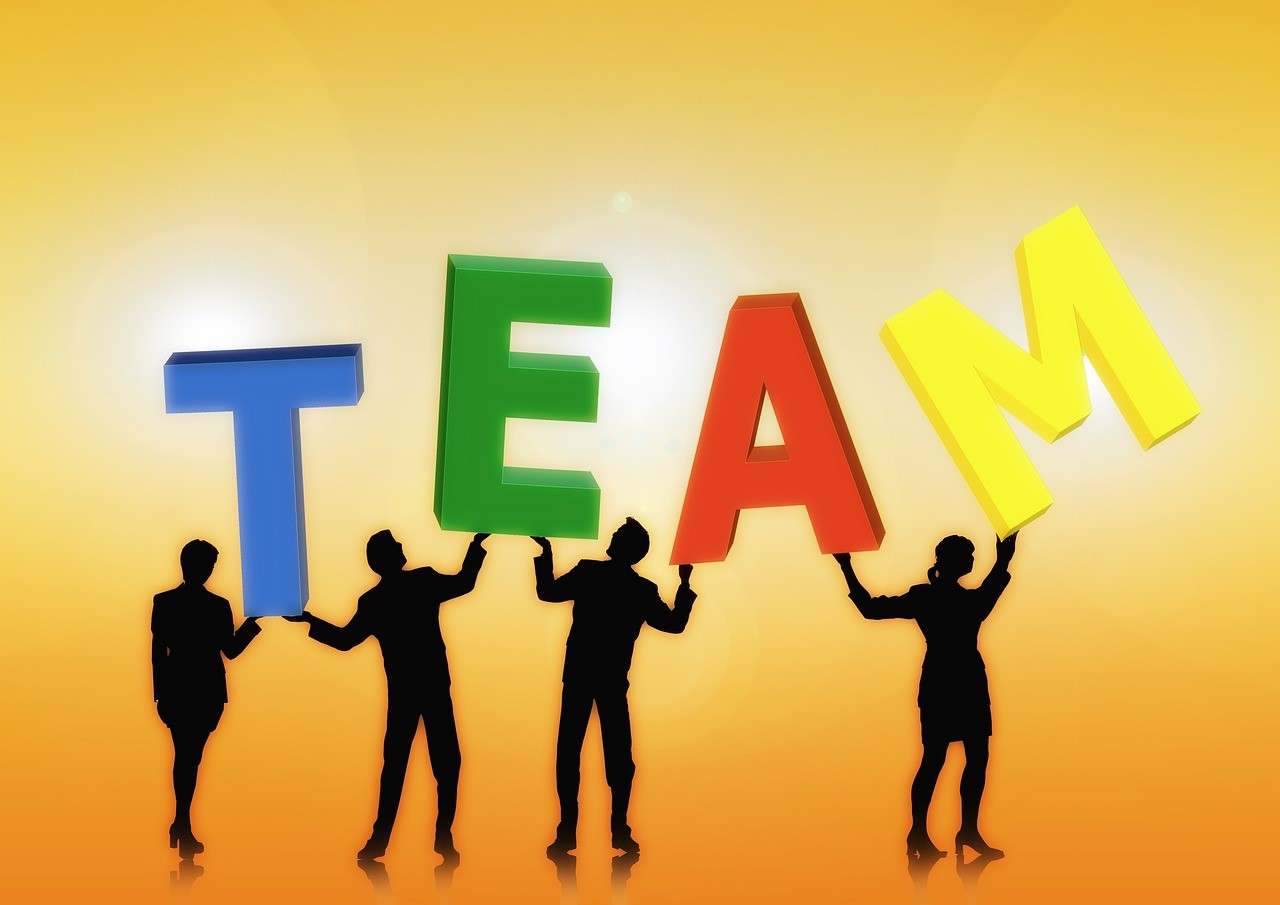People in silhouette against a yellow background holding multi-colored letters that spell "team"